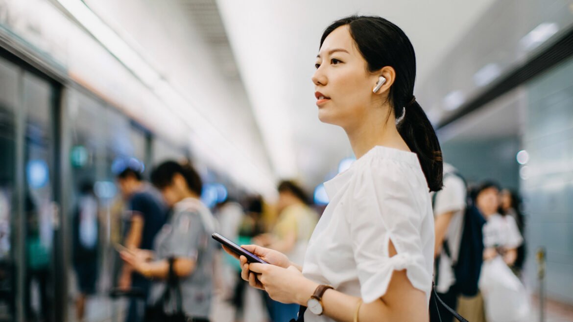Young woman carrying shopping bag using smartphone while waiting for subway in platform