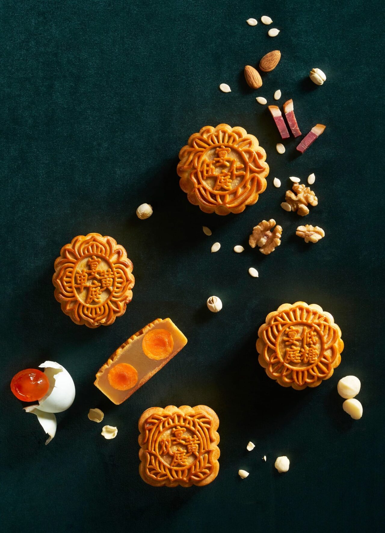 Assorted baked mooncakes with egg yolks, nuts, seeds and ham on a dark green background
