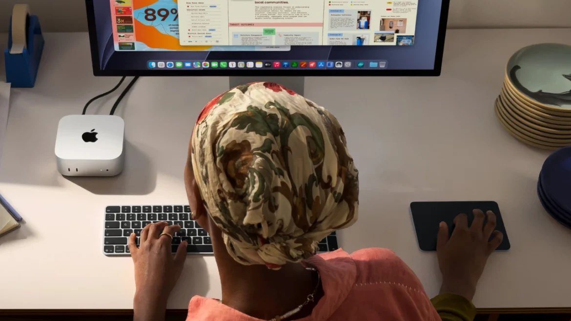 An overhead view of a person using a keyboard and mouse at a desk, with a Mac mini connected to a large display.