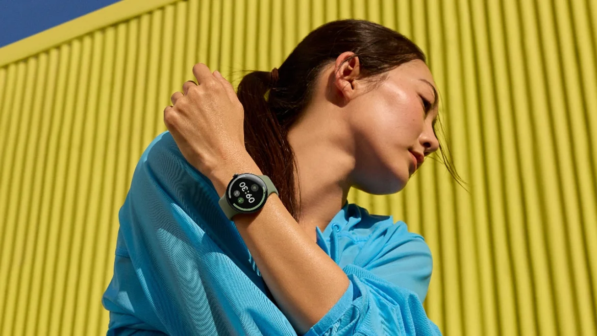 Person wearing an Olive Google Pixel Watch 5 outdoors against a yellow wall.